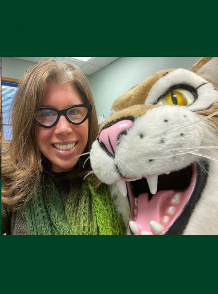 Portrait of a woman in green, smiling with a stuffed toy tiger. 